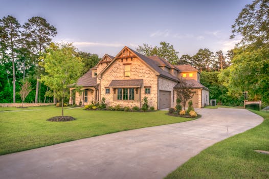Elegant stone family home surrounded by trees, lush lawn, and vibrant garden.